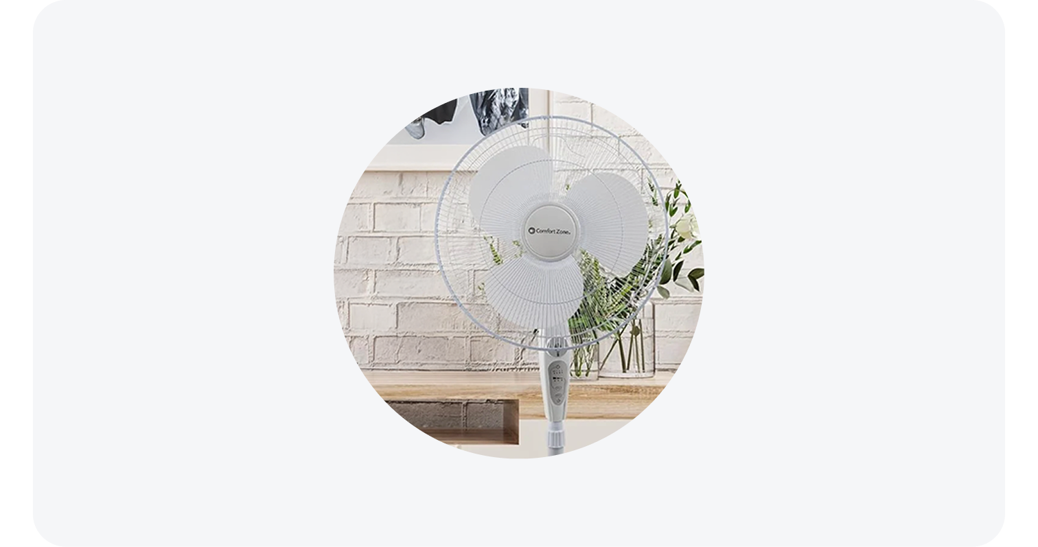 Comfort Zone white oscillating fan in a home setting in front of a brick wall and flowers.