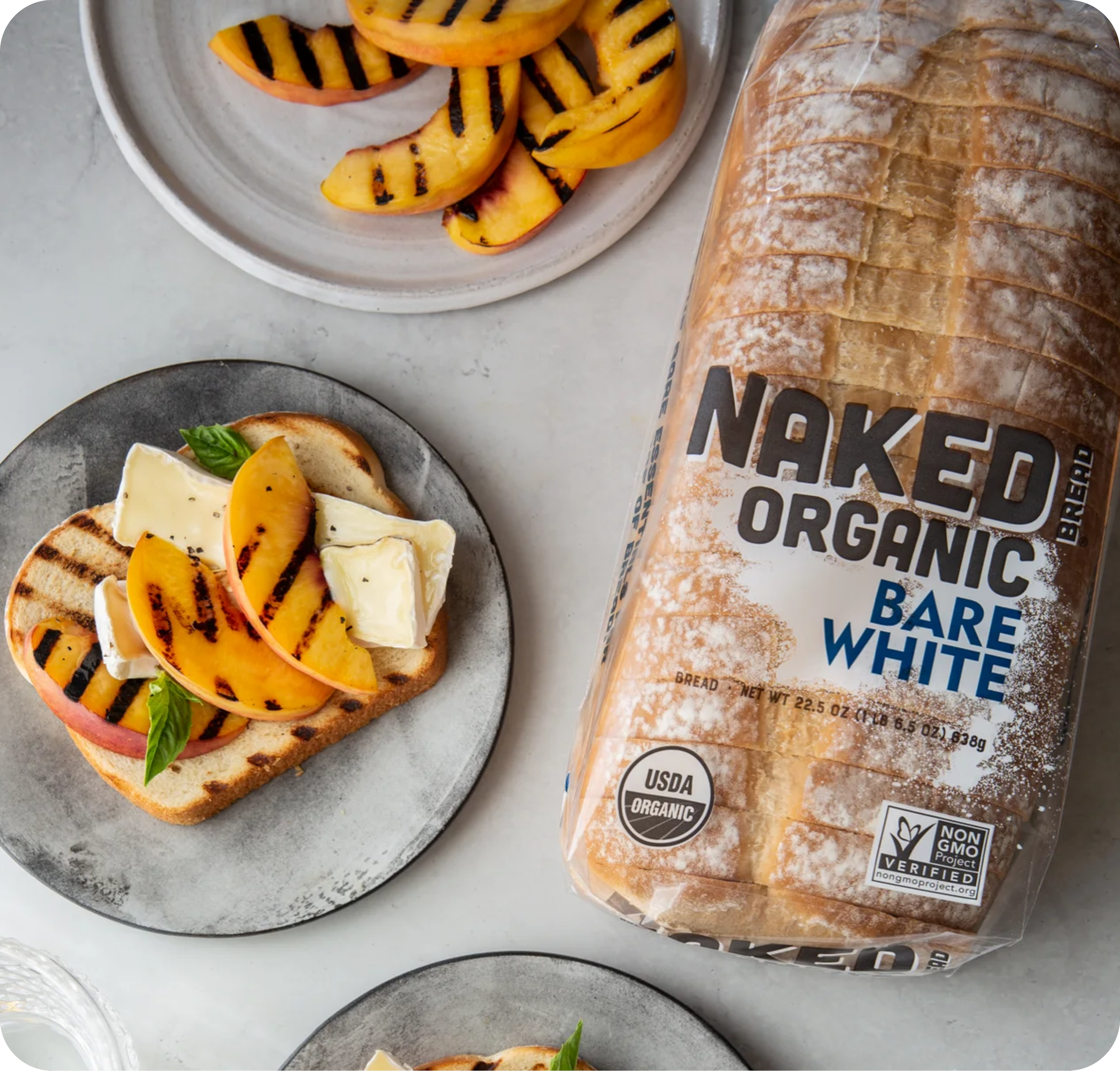 Naked Organic Bare White bread loaf next to toast topped with grilled peaches and cheese.